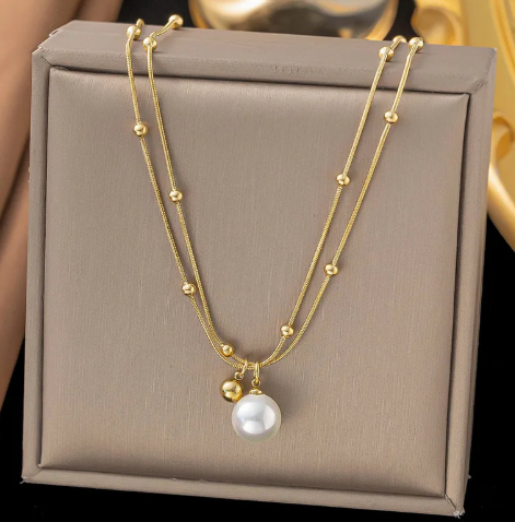 Collar doble con bolitas en la cadena y dijes dorado y perla.