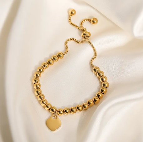 Pulsera de bolitas con dije de corazón, ajustable. Color dorado.